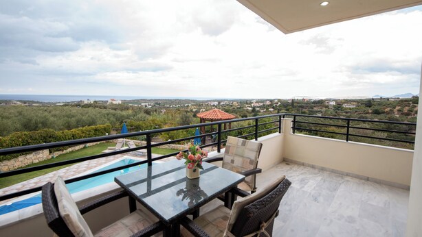 Ein Balkon mit Glastisch, Korbstühlen und Blick auf Pool und Landschaft.