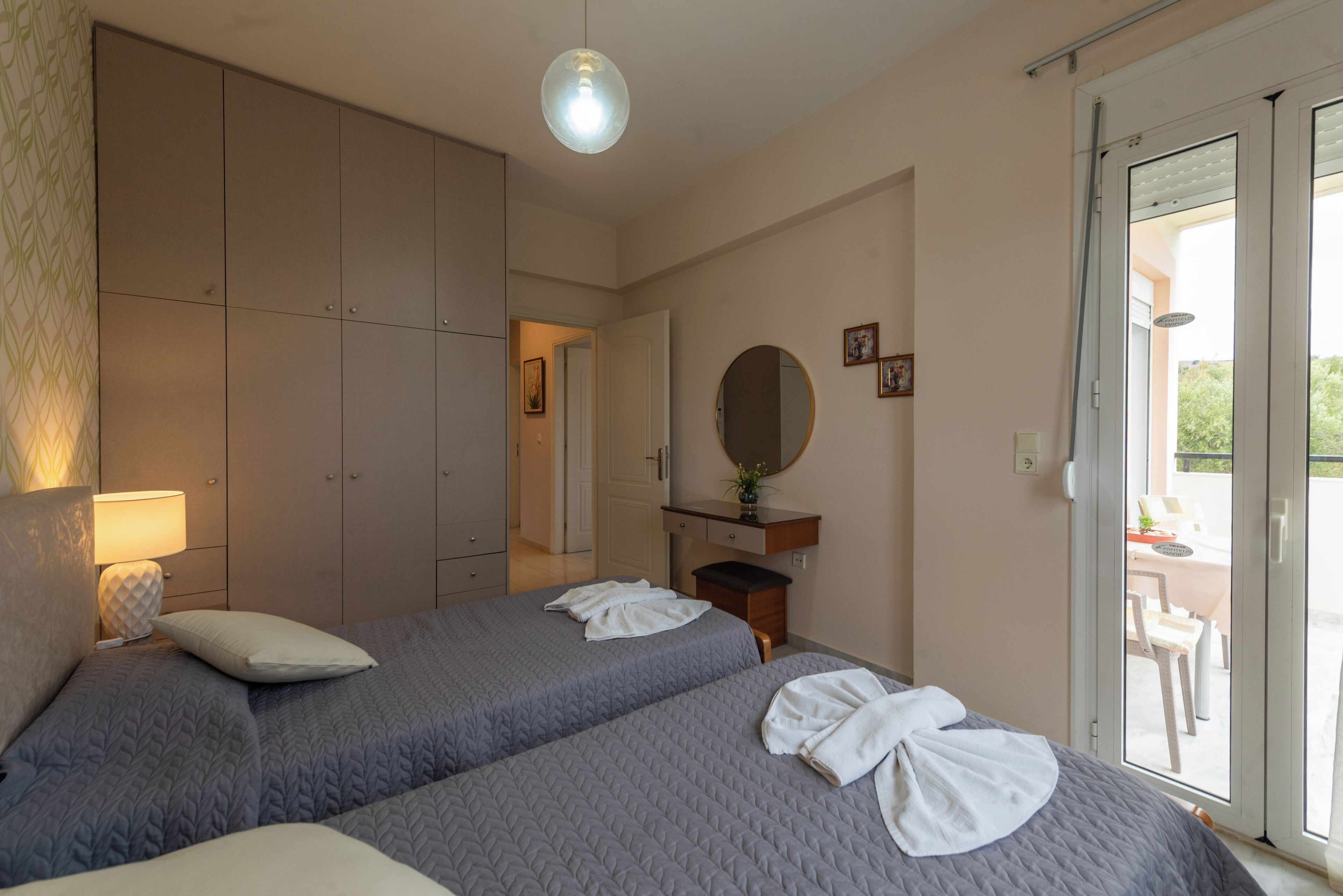 Un dormitorio con dos camas, un aparador, un espejo y una puerta corredera de vidrio que da a un espacio al aire libre.