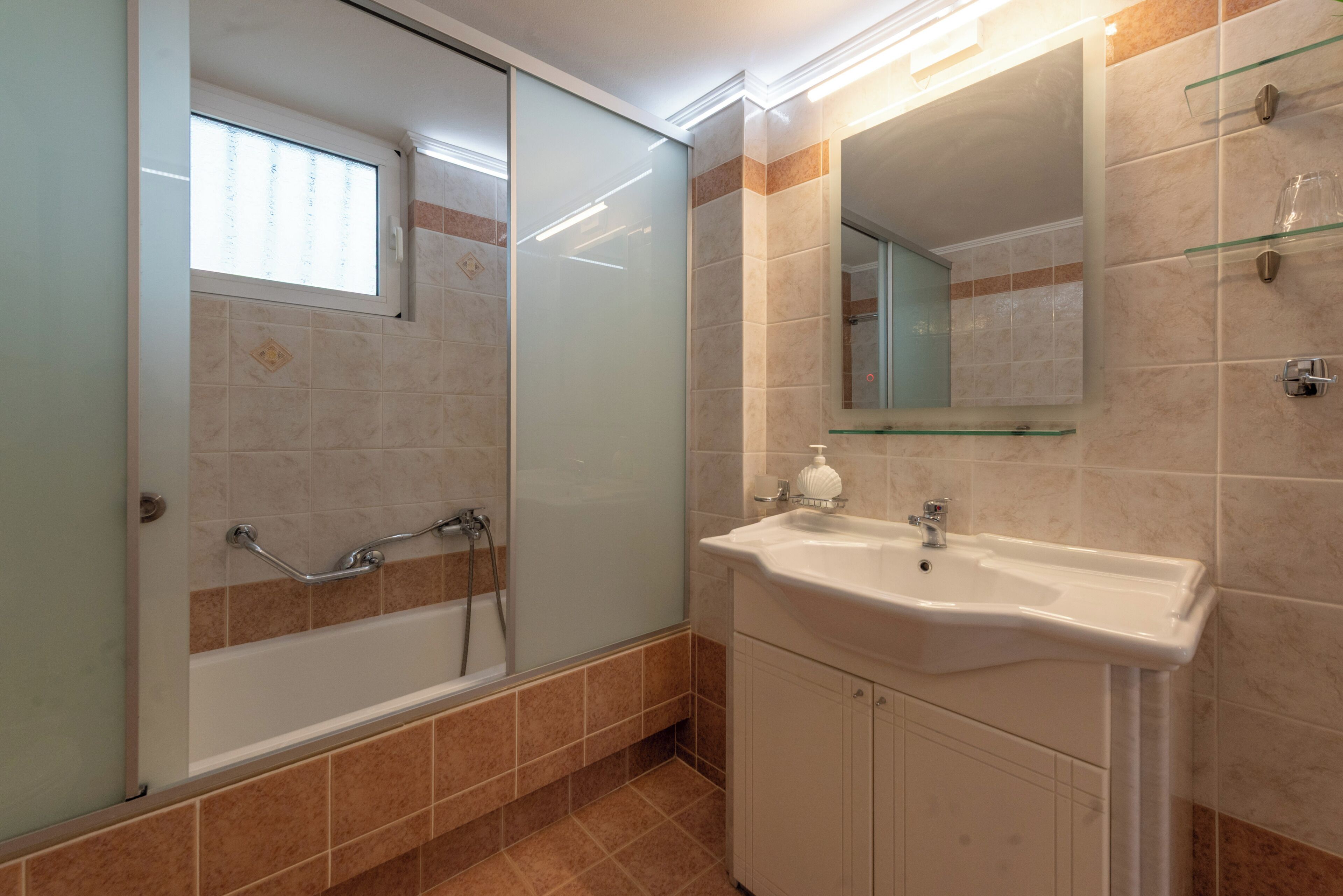 Un bagno con cabina doccia in vetro, un lavabo con specchio e pareti rivestite in piastrelle.