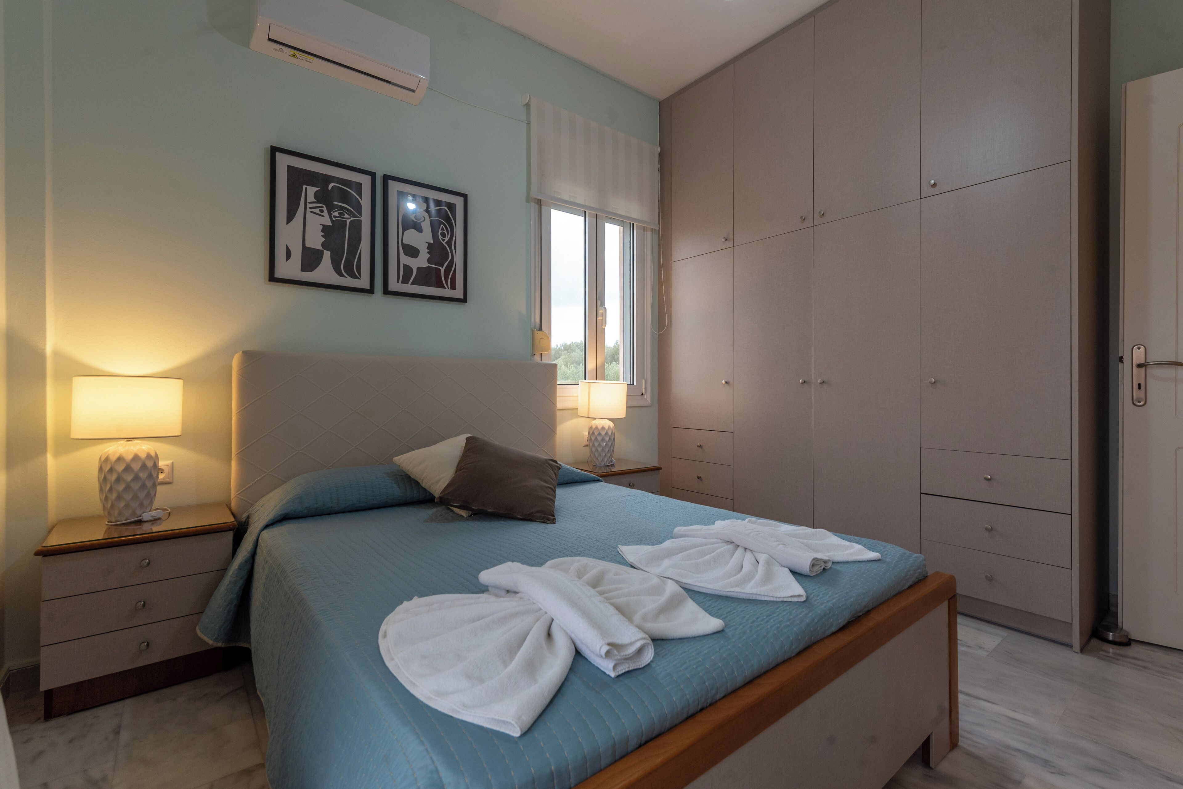 A bedroom with a bed, two bedside tables, a wardrobe, and artwork on the wall.