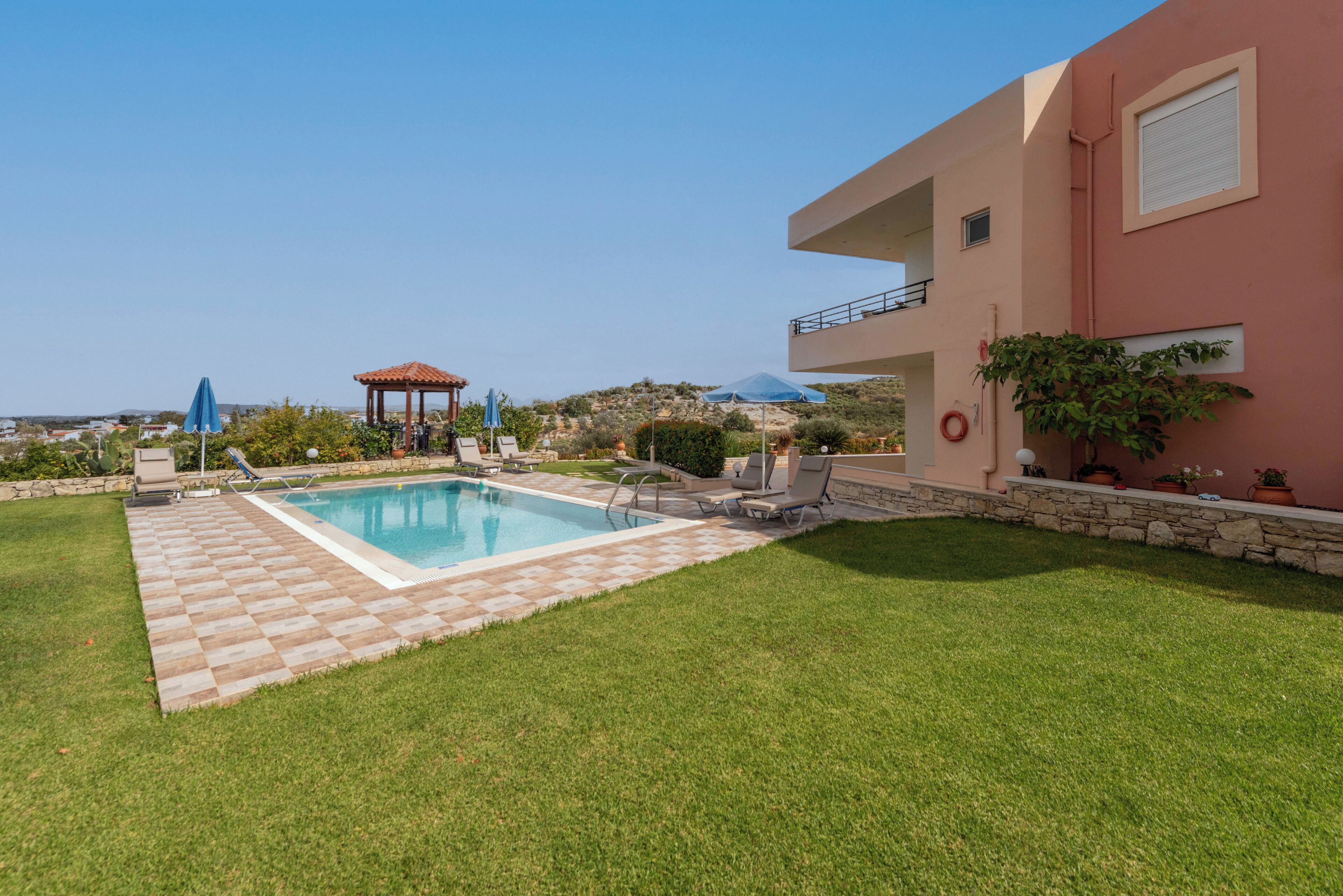 A swimming pool with lounge chairs and umbrellas, surrounded by a well-maintained lawn and a stone wall.