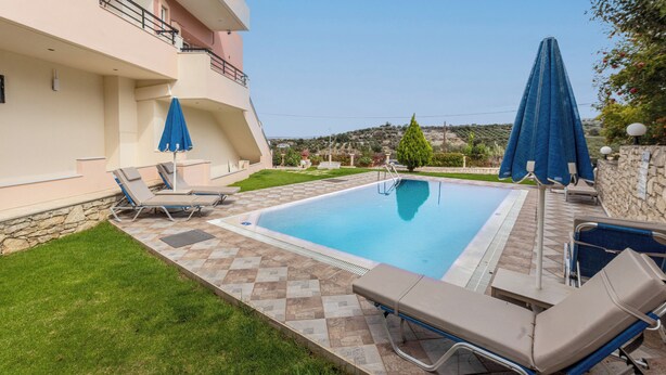A swimming pool with lounge chairs and umbrellas, surrounded by a stone wall and a grassy area. - Villa Pantelis With Private Pool (Rethymno)