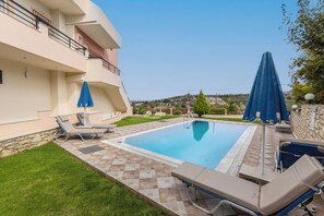 Une piscine entourée d’un mur de pierre et d’une pelouse, avec des chaises longues et des parasols à proximité.