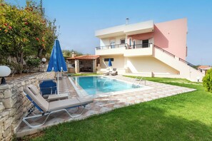 A two-story building with a swimming pool, outdoor seating, and a stone wall. - Villa Pantelis With Private Pool (Rethymno)