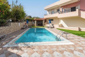 A swimming pool with a stone wall and lounge chairs. - Villa Pantelis With Private Pool (Rethymno)