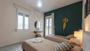 A hotel room with two beds, a mirror, a window, and a wall-mounted air conditioner. - Villa Pantelis With Private Pool (Rethymno)