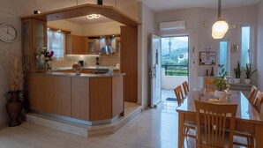 A modern kitchen with wooden cabinets, a central island, and a dining area with a glass table and wooden chairs. - Villa Pantelis With Private Pool (Rethymno)