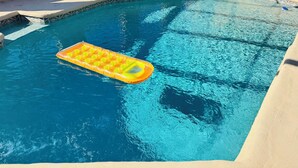 A swimming pool with a floating mat, a blue chair, and a hose on the deck. - 5/3 Pool Home In Central Lakeland, Pet Friendly! (Lakeland)