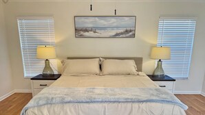 A bedroom with a large bed, two bedside tables with lamps, a painting on the wall, and a window with blinds. - 5/3 Pool Home In Central Lakeland, Pet Friendly! (Lakeland)