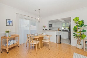 A modern kitchen with white cabinets, a dining area with a round table and chairs, a wicker side table with towels, and a potted plant. - 3-bedroom house in marvelous North Myrtle Beach - Cozy and Modern (North Myrtle Beach)