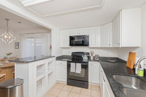 A modern kitchen with white cabinetry, a black microwave, a stove, and a granite countertop. - 3-bedroom house in marvelous North Myrtle Beach - Cozy and Modern (North Myrtle Beach)