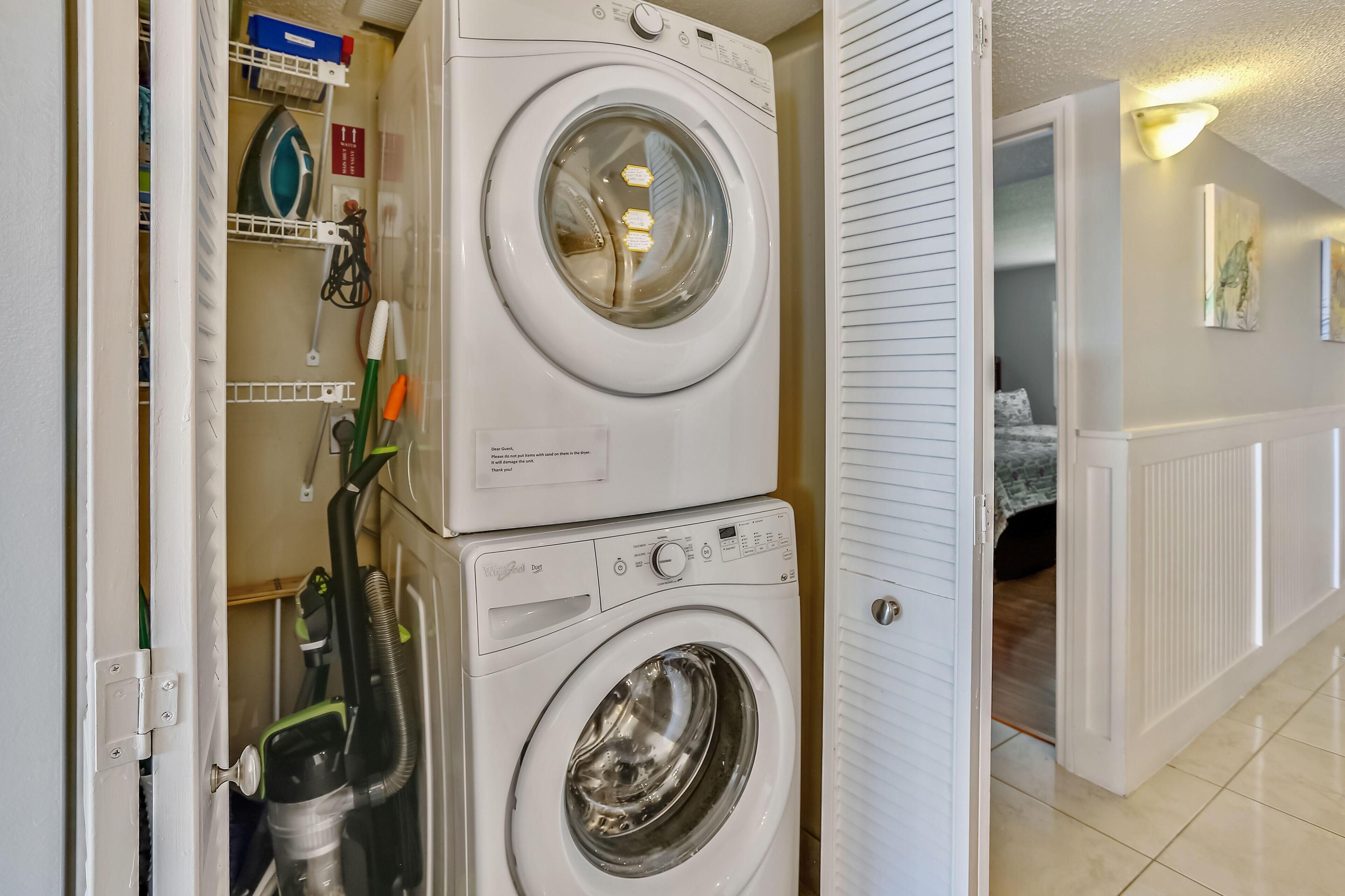 A laundry room with stacked washing machines and a vacuum cleaner.
