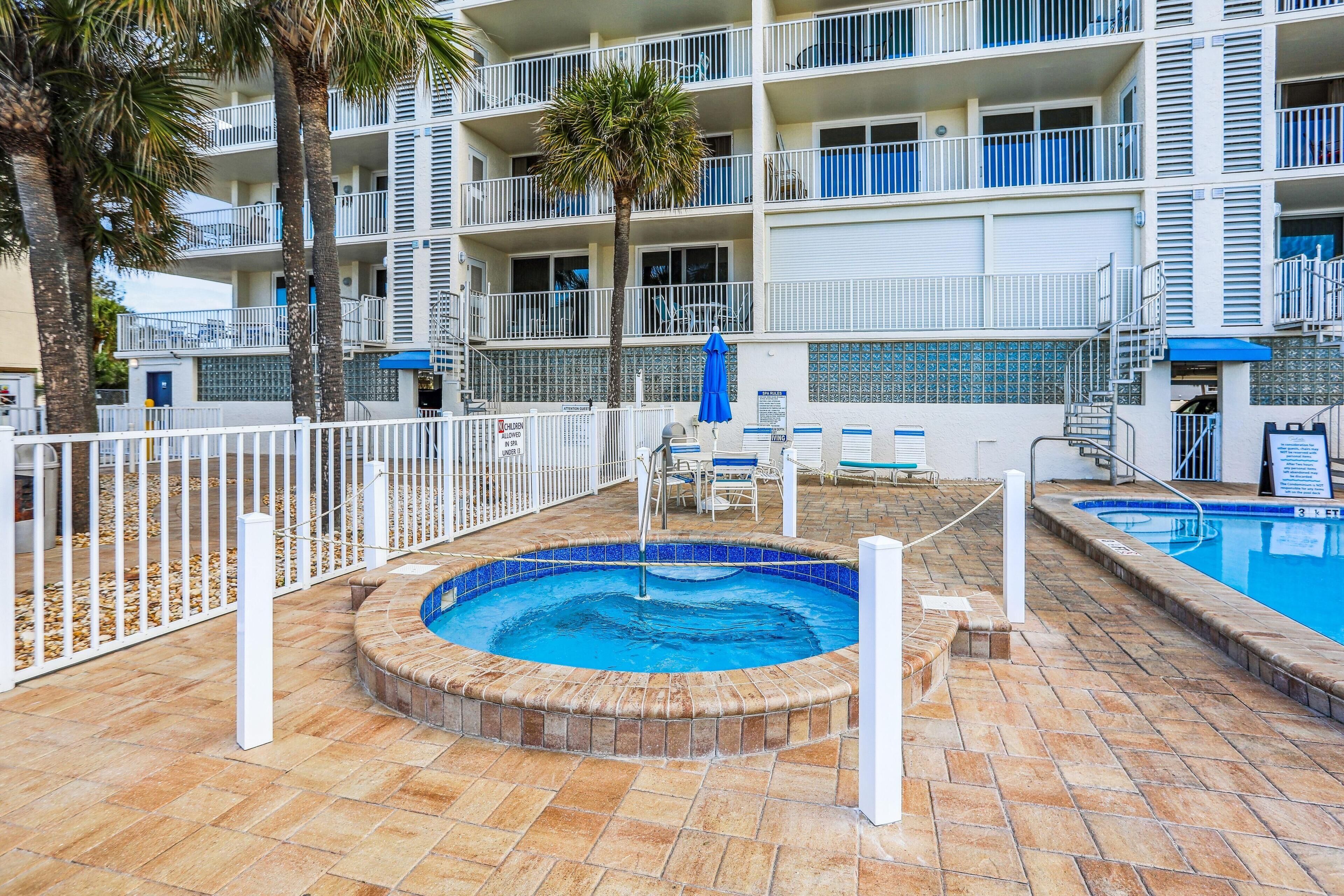 A pool area with a hot tub, palm trees, and a white fence.