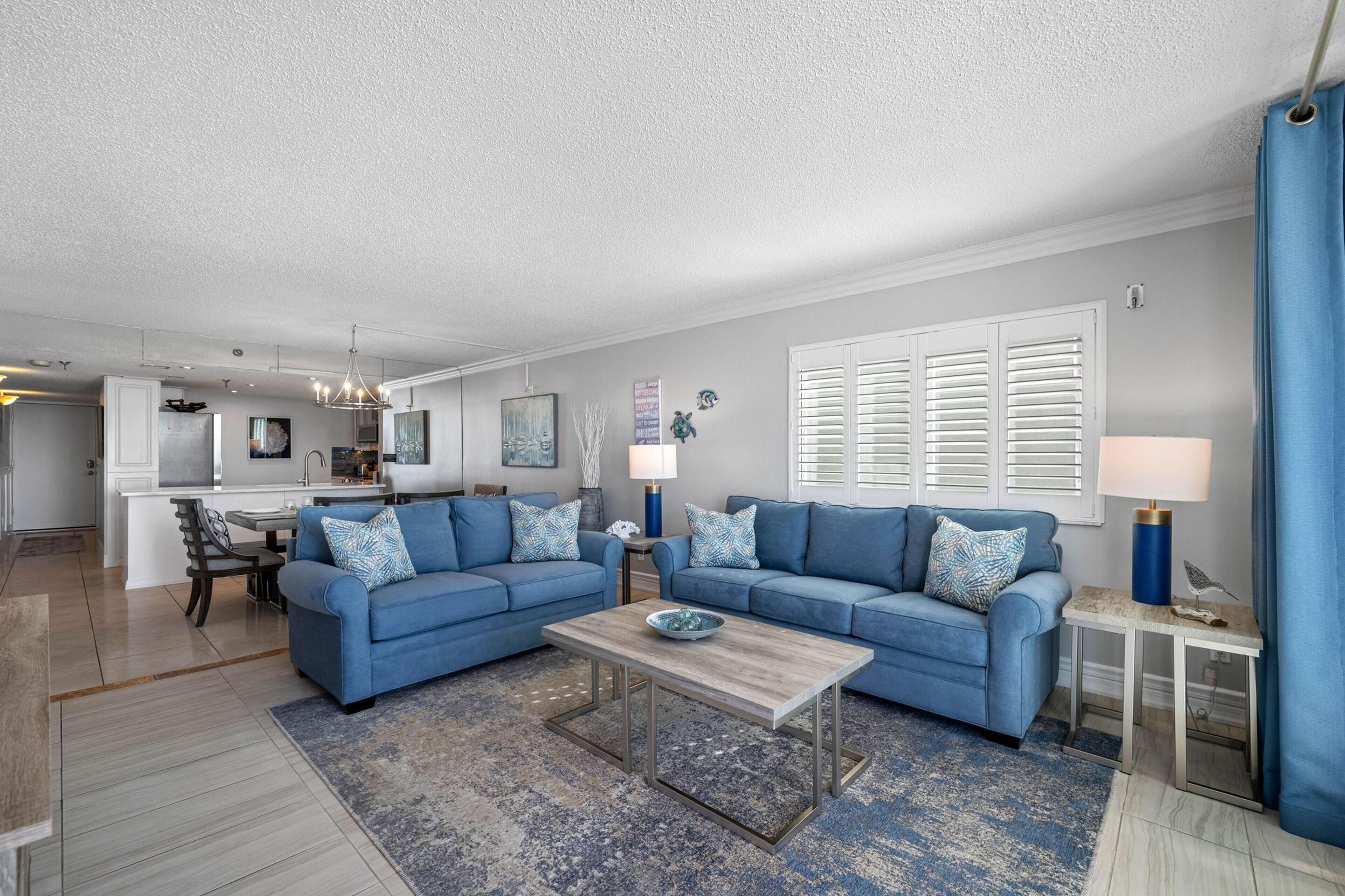 A modern living room with a blue sofa set, a coffee table, and a kitchen in the background.