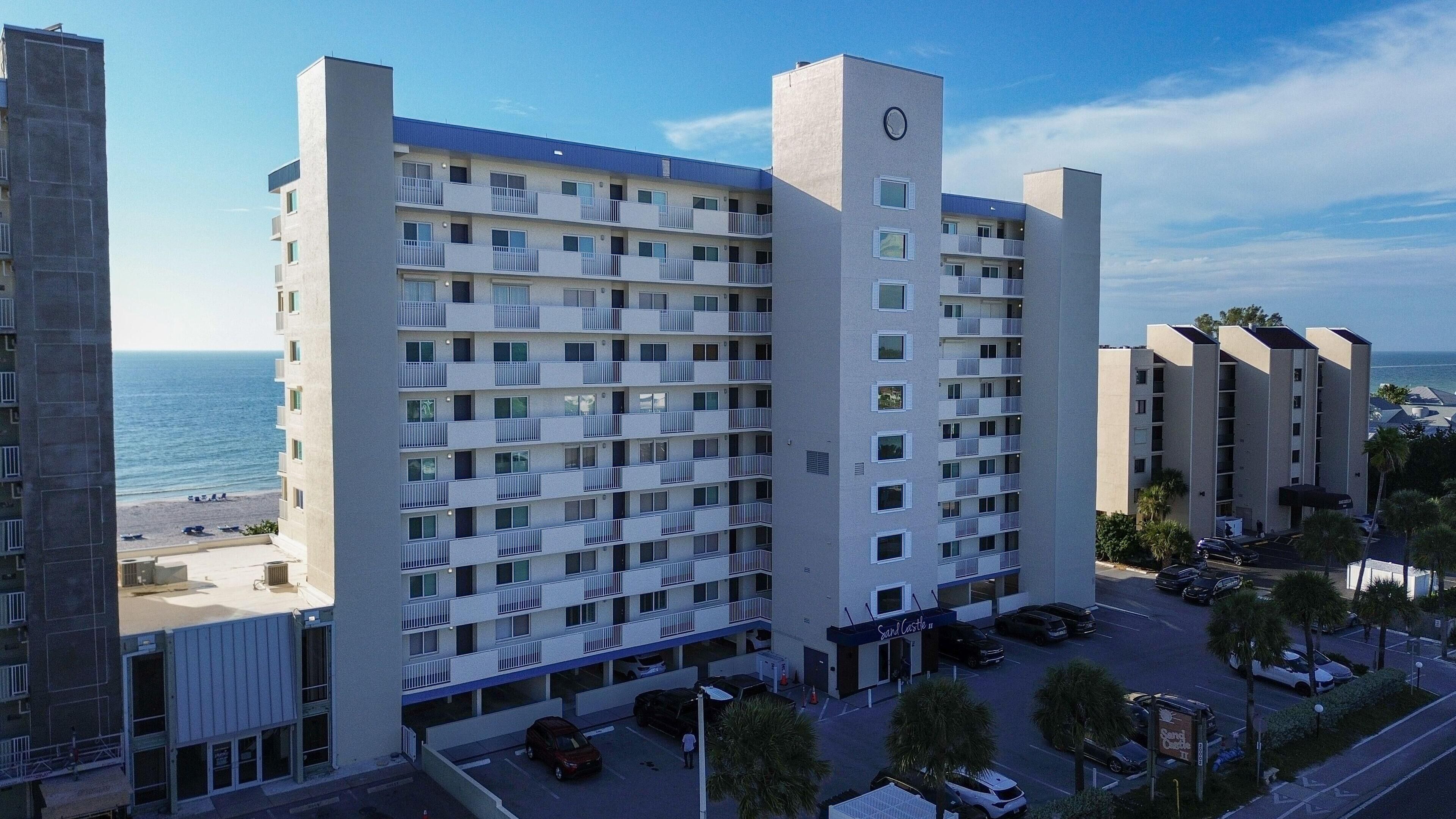 Un hotel de varios pisos con balcones, zona de estacionamiento y vista a la playa.