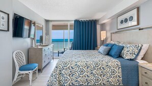 Un dormitorio con una cama grande, un aparador, una silla y vista al océano.