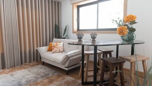 A modern living room with a sofa, a coffee table, and two wooden stools. There is a window with curtains, a vase with flowers, and a plant. - Estrelas do Douro (Gondomar)
