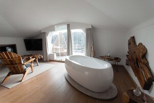 Un baño moderno con una bañera independiente, suelo de madera y un amplio ventanal con cortinas.