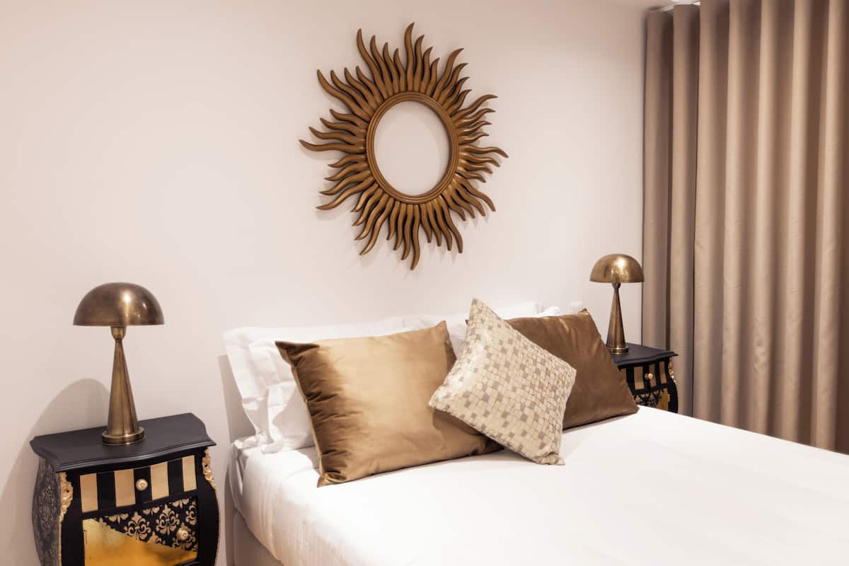 A neatly made bed with two pillows, a decorative wall mirror, and two bedside tables with lamps.
