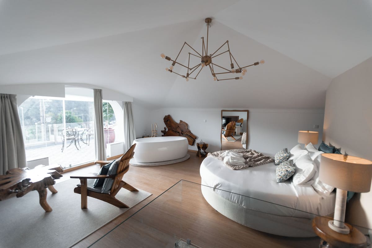 A modern bedroom with a large bed, a wooden chair, a glass coffee table, and a unique chandelier.