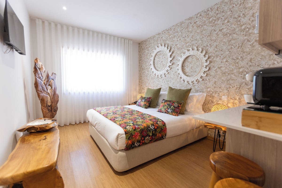 A modern bedroom with a large bed, a wooden bench, a TV, and decorative wall mirrors.