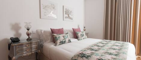 Un dormitorio ordenado con una cama, dos mesitas de noche y dos obras de arte colgadas en la pared.