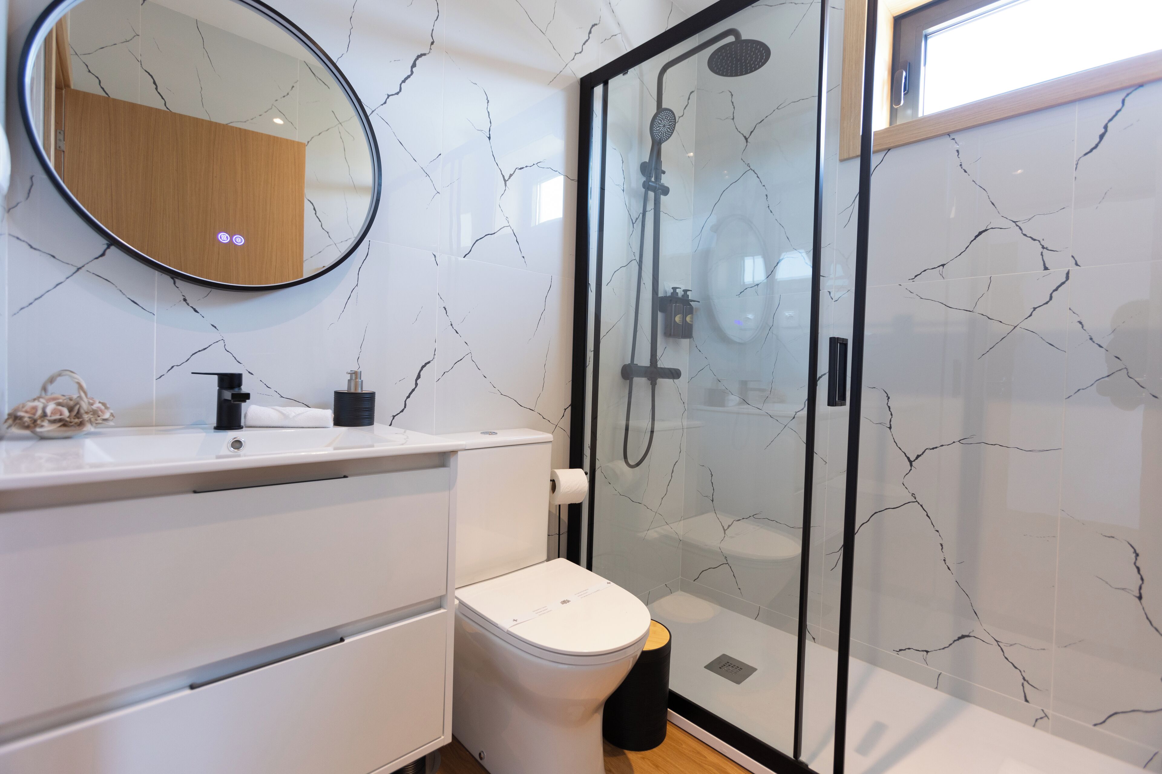 Een moderne badkamer met een douchecabine van glas, een wit toilet en een wand met een marmerlook.