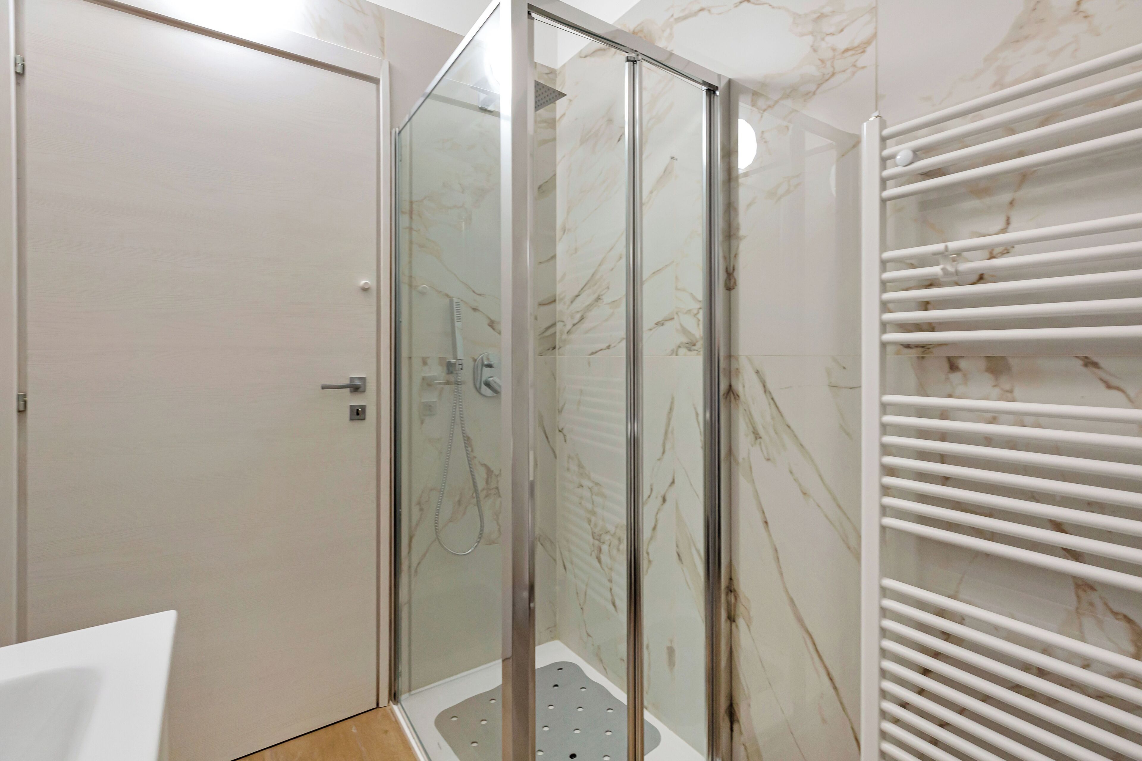 Ein modernes Badezimmer mit einer gläsernen Duschkabine, einem weißen Handtuchhalter und Marmorwänden.
