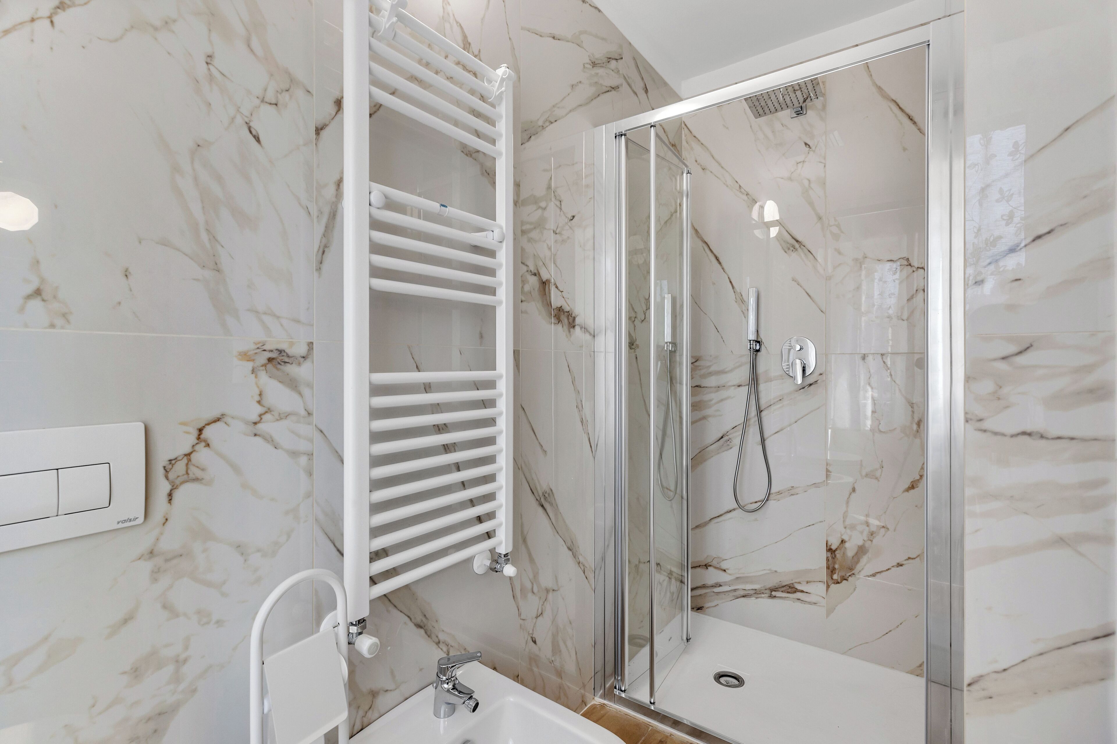 A modern bathroom with a glass-enclosed shower, a white bathtub, and a marble backsplash.