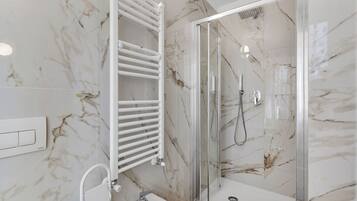 A modern bathroom with a glass-enclosed shower, a white bathtub, and a marble backsplash.