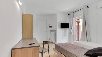 Un dormitorio con cama, escritorio, silla, televisor y ventana con cortinas.
