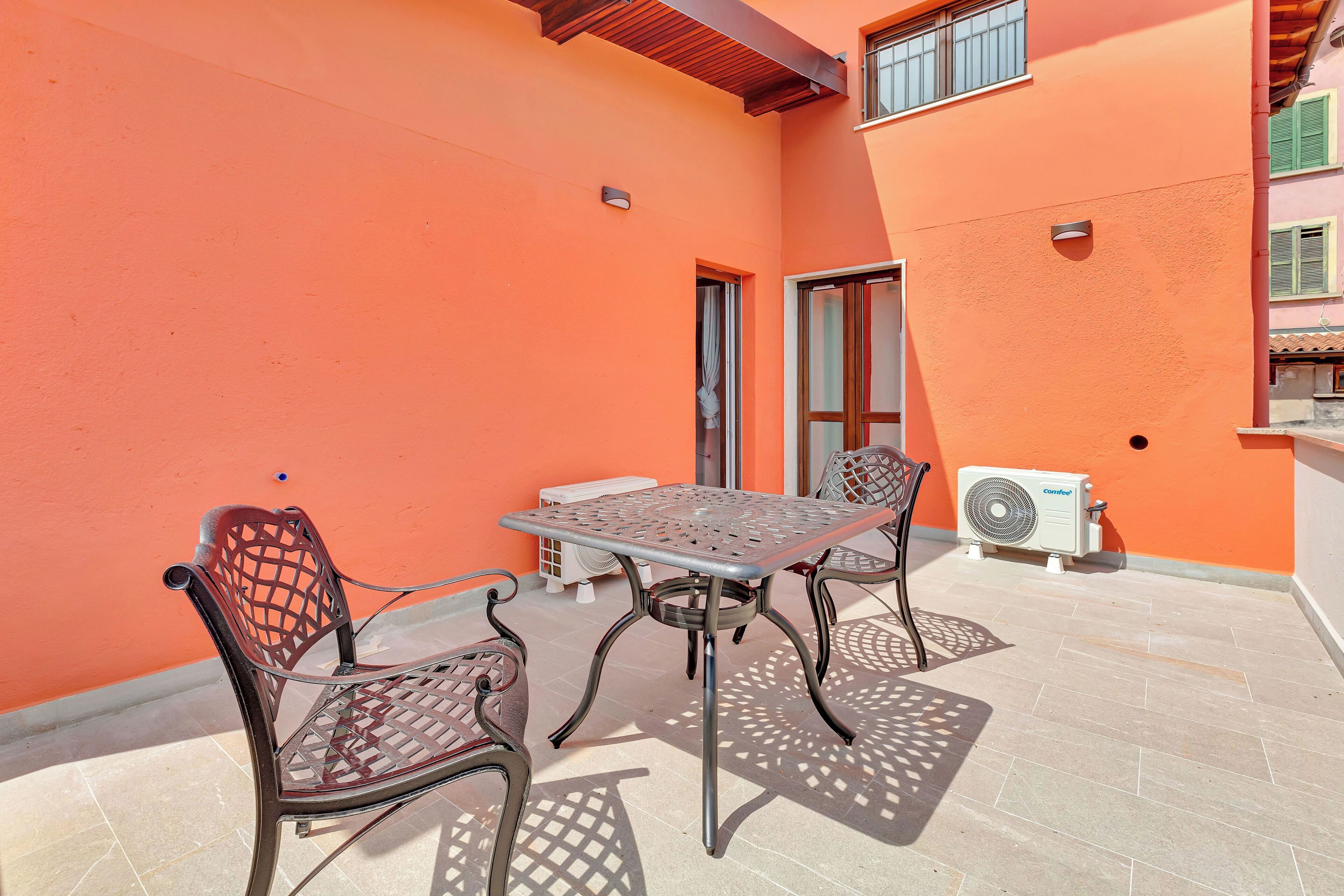 Une terrasse extérieure avec une table et des chaises en métal, un climatiseur blanc et un sol carrelé.