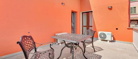 Une terrasse extérieure avec une table et des chaises en métal, un climatiseur blanc et un sol carrelé.