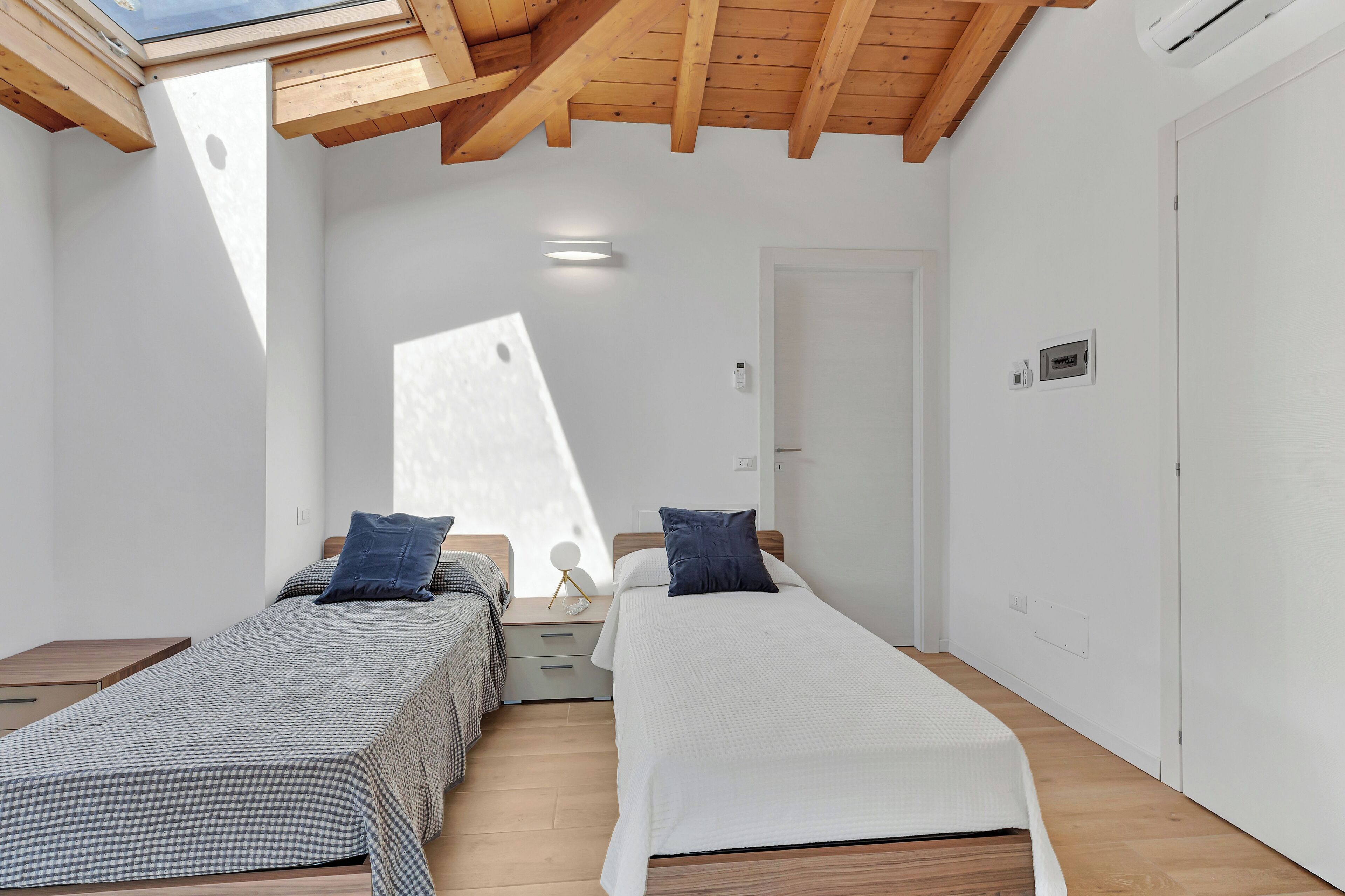 Une chambre avec deux lits, un plancher en bois, un puits de lumière et une porte blanche.
