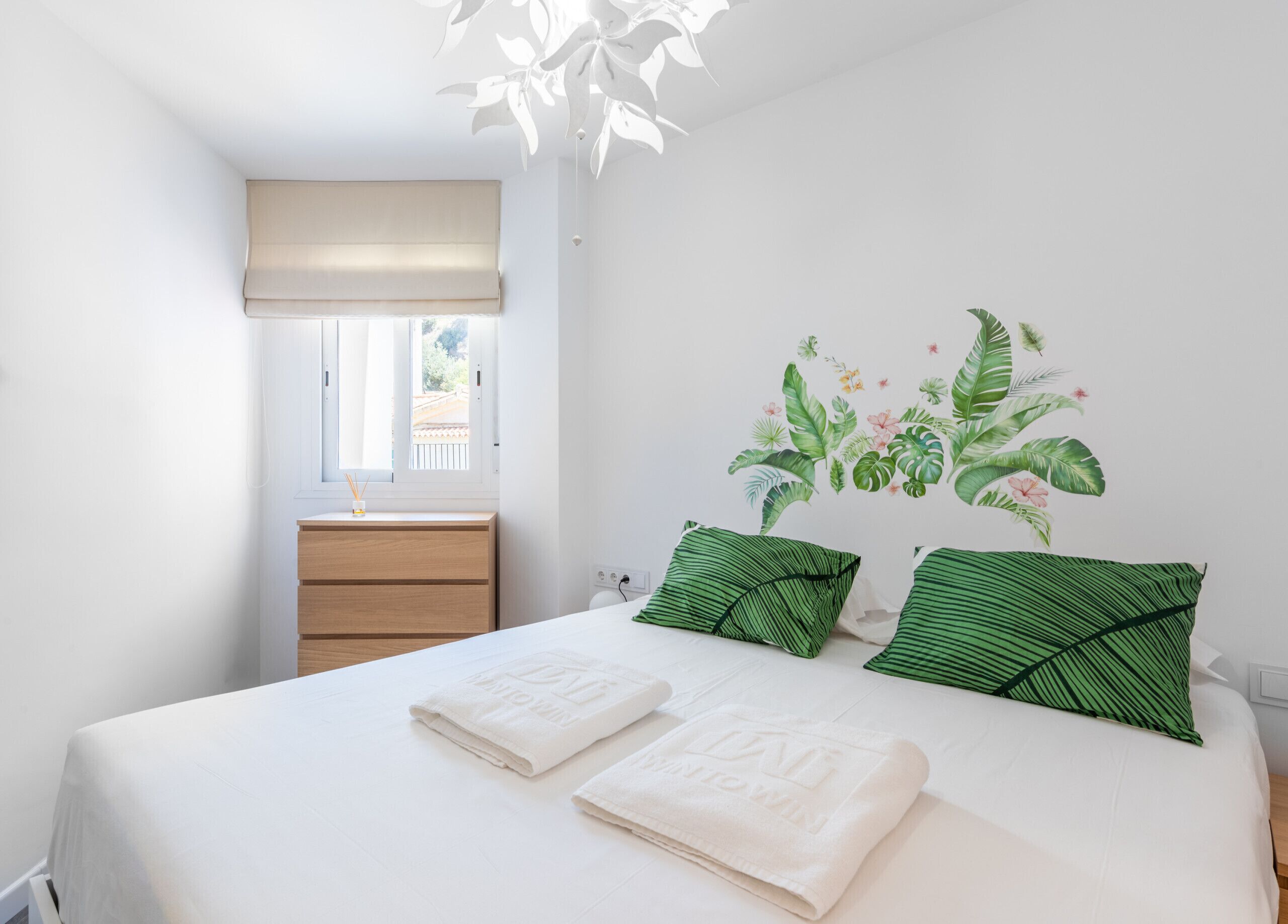 Una camera da letto con un letto, due cuscini, un comodino, una finestra vista e una decorazione a parete.