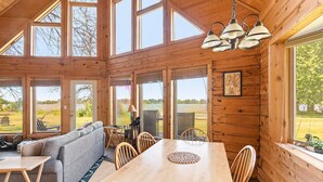 Uma cabana espaçosa com uma grande mesa de jantar, paredes de madeira e amplas janelas com vista para o exterior.