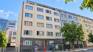 Un edificio residencial de varios pisos con fachada plana, múltiples ventanas y una parada de autobús a nivel de calle.