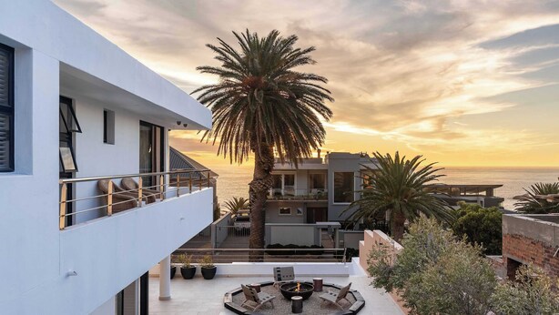 Un edificio moderno con un patio sul tetto, arredato con mobili da esterno, un braciere e vista sull'oceano al tramonto.