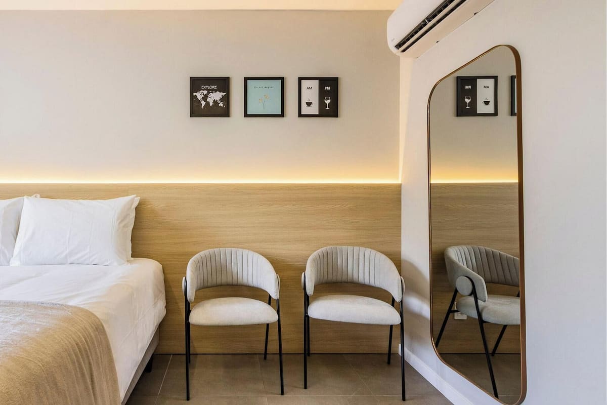 A hotel room with a bed, two chairs, a large mirror, and wall art depicting a world map and time-related icons.