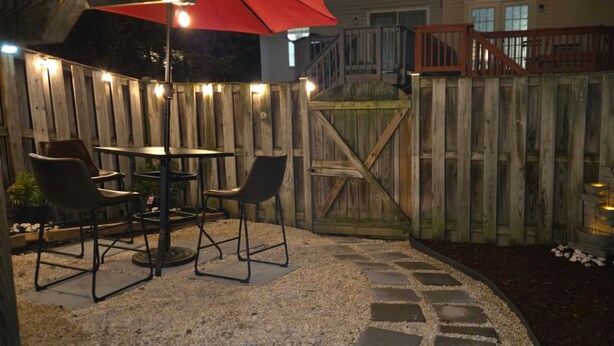 An outdoor patio with a wooden fence, a table with chairs, and a red umbrella. - Charming Retreat in the Heart of the City (Springfield)