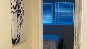 A bedroom with a wooden floor, a bed with a blue bedspread, a window with blinds, and a leopard print artwork on the wall. - Charming Retreat in the Heart of the City (Springfield)