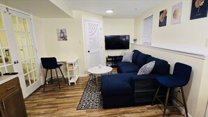 A compact living space with a sofa, a small round table, a TV, and a kitchen area with cabinets and a countertop. - Charming Retreat in the Heart of the City (Springfield)