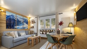 A modern living room with a sofa, coffee table, and dining area with chairs. - Petit Social - Chaleureux | 4pax | Vue Montagne | Remontée300m (Chamonix-Mont-Blanc)