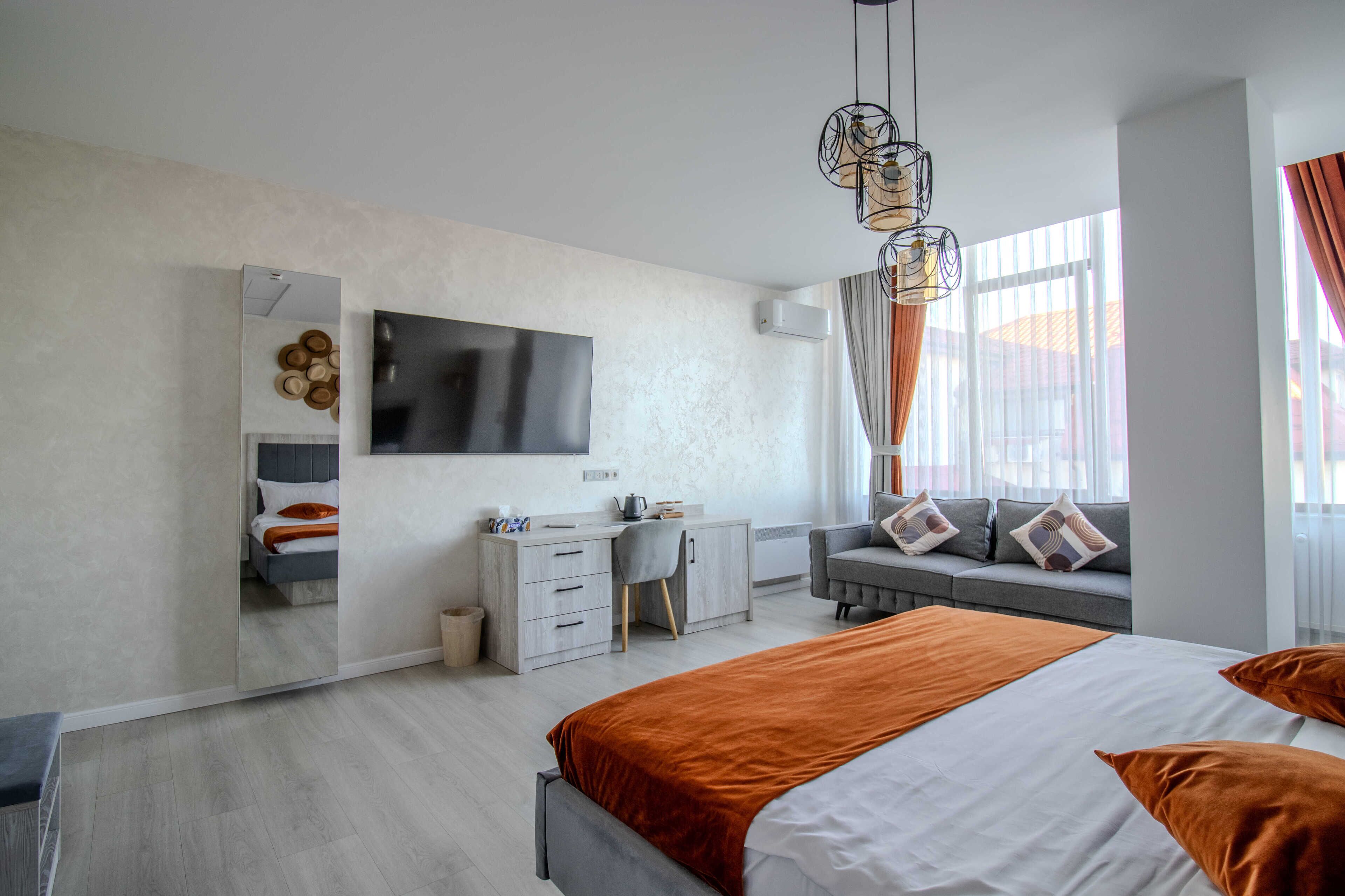 A modern hotel room with a large bed, a desk, a chair, a TV, and a window with curtains.