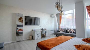 A modern hotel room with a large bed, a desk, a chair, a TV, and a window with curtains.