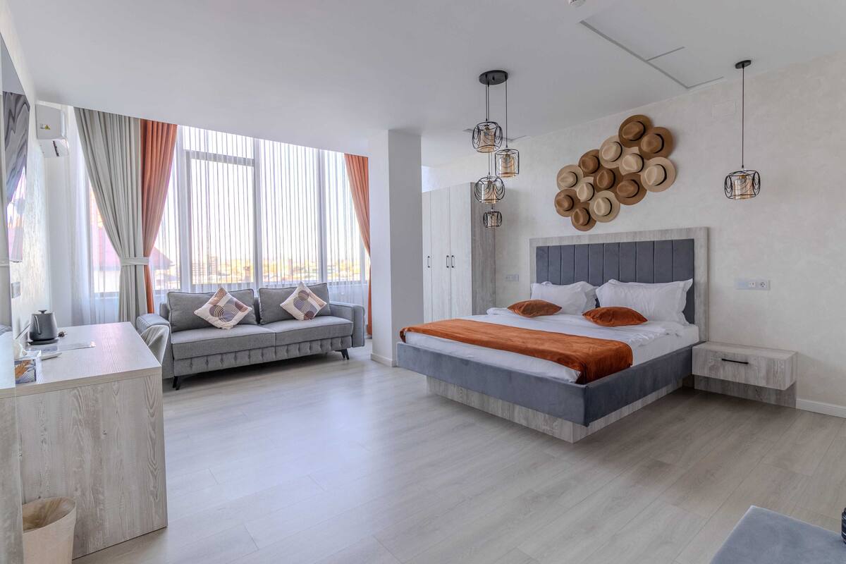 A modern bedroom with a bed, a sofa, a desk, and a wall-mounted hat display.