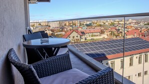 A balcony with wicker furniture and a glass table, overlooking a cityscape with buildings and solar panels. - Casa Munteneasca Alessandro (Bradu)