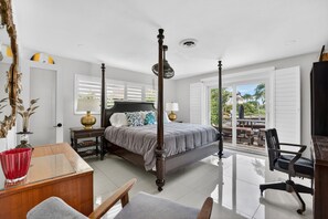 A four-poster bed with a nightstand, a desk with a chair, and a view of the outdoor patio. - Minutes to Marlin! Sailor's Cove at Santa Barbara Shores...Now Available! (Pompano Beach)