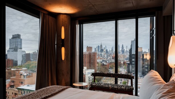 A hotel room with a large window, a bed, a chair, and a small table. - The Merchant Hotel Lower East Side (New York)