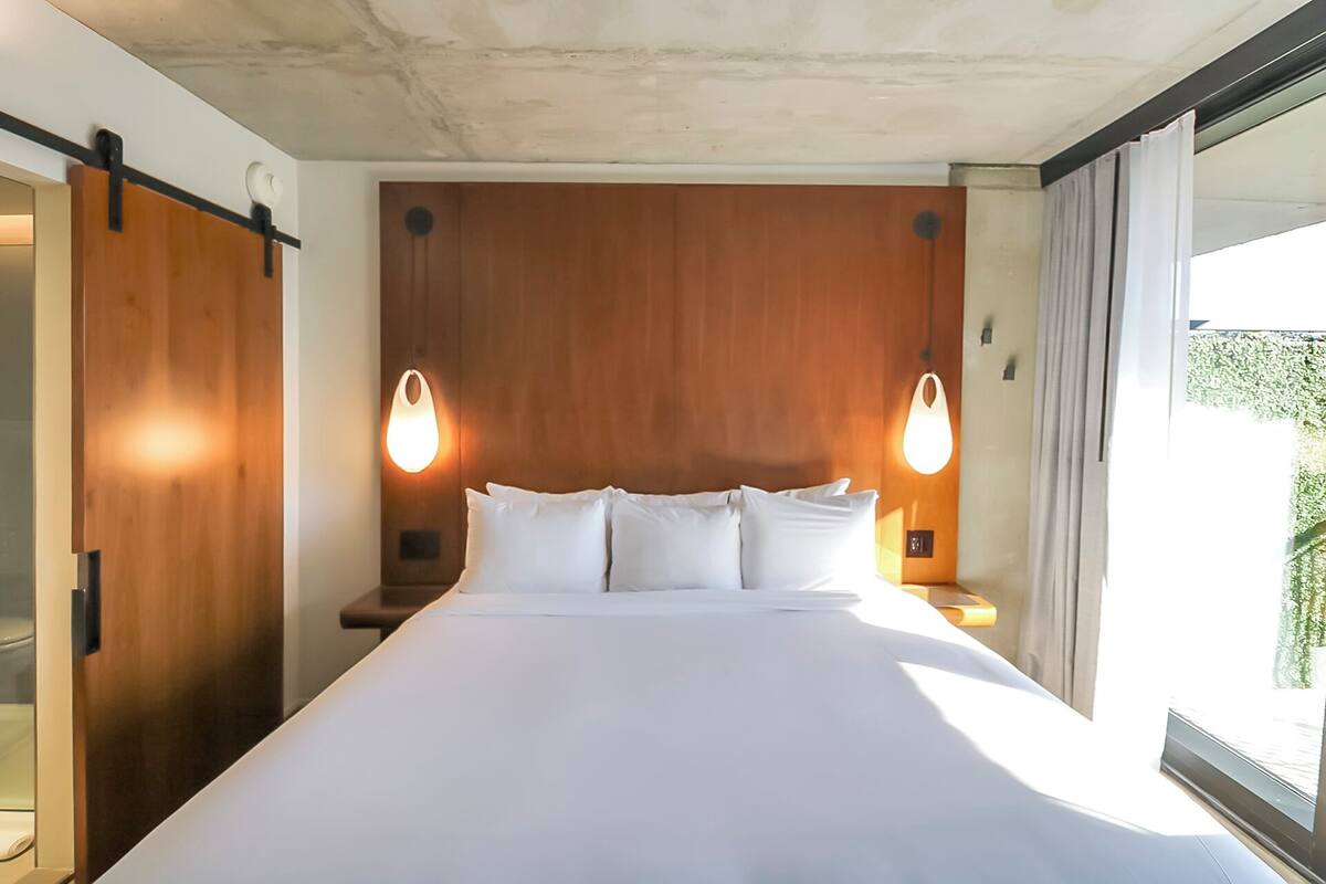 A modern hotel room with a large bed, wooden headboard, and two wall-mounted lamps.